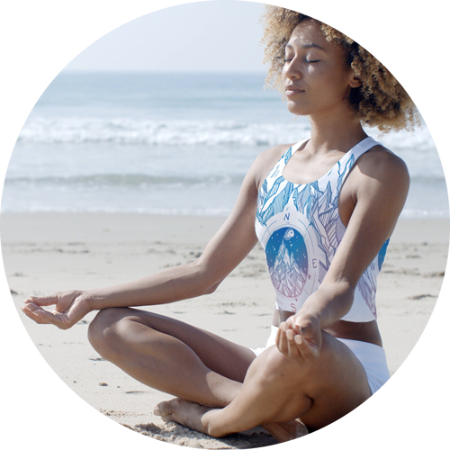 Picture of a girl meditating on a beach, wearing a custom printed athletic crop top