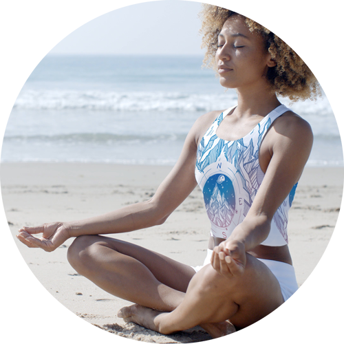 Picture of a girl meditating on a beach, wearing a custom printed athletic crop top